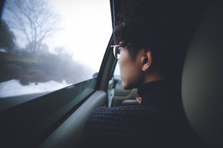 a woman with glasses sitting in a car looking out the window.