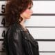 a woman in a leather jacket standing in front of a mugshot.