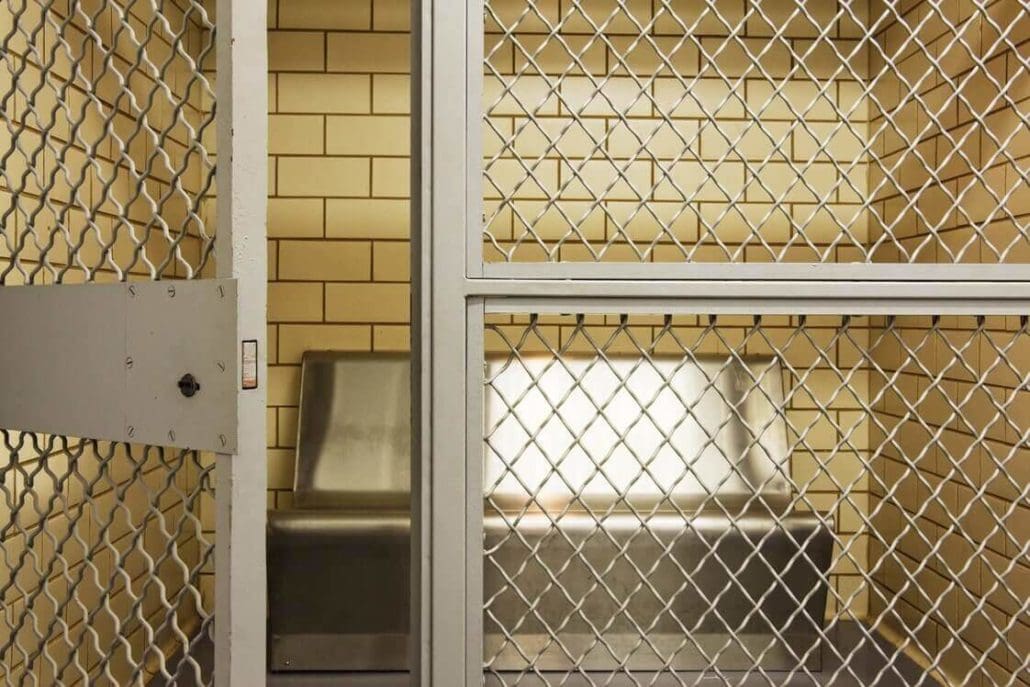 a jail cell with a metal door and a bench.
