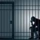 a man sitting on a bench in a jail cell.