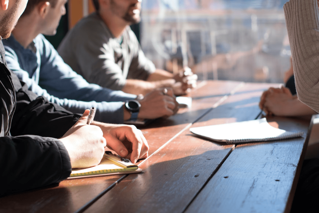 a group of people sitting around a wooden table.