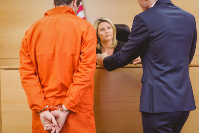 A man in an orange prison suit is talking to a woman in a courtroom.