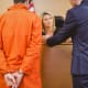 A man in an orange prison suit is talking to a woman in a courtroom.