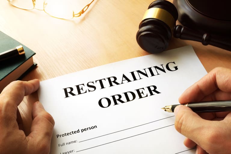 A hand writing a restraining order on a piece of paper.