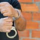 A man with handcuffs holding a brick wall.