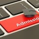 A graduation cap sits on a red button on a computer keyboard.