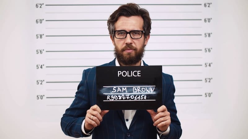 Guilty businessman in police station posing for mugshot with placard. Mug shot of bearded bribe taker holding board and looking at camera with height scale on background