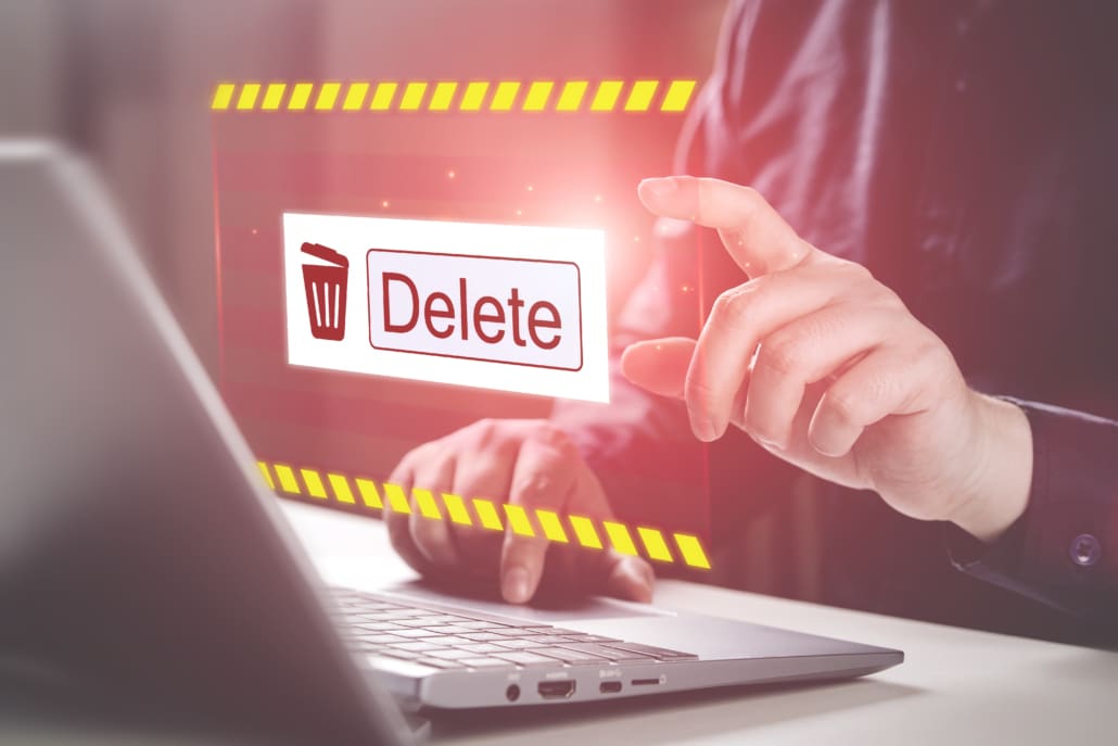 A person interacting with a virtual delete button on a digital interface above a laptop, symbolizing file deletion or data management.